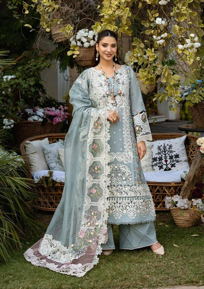 Woman in a light blue embroidered traditional outfit standing in a decorative outdoor setting with flowers and furniture.