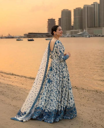 Woman in a blue and white floral dress standing on a beach with city skyline in the background